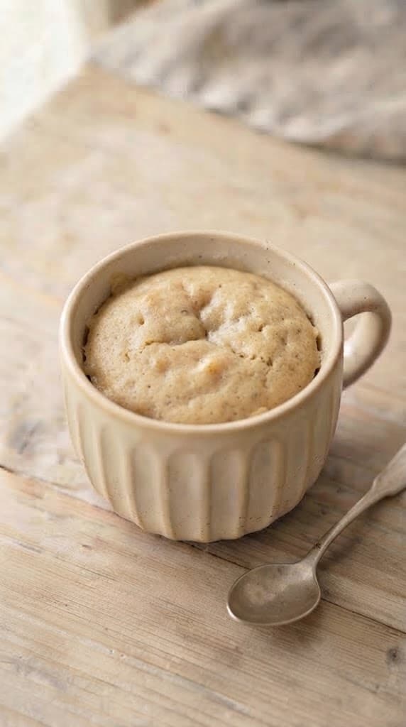 Freshly microwaved banana mug cake with a warm golden color, soft risen top, and moist tender crumb in a cream ceramic mug