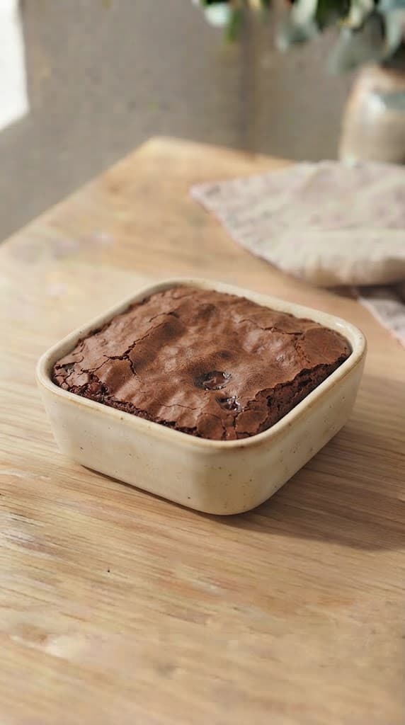 Freshly baked egg-free brownie in a small square ceramic baking dish with set edges, a crackled top, and a soft fudgy center