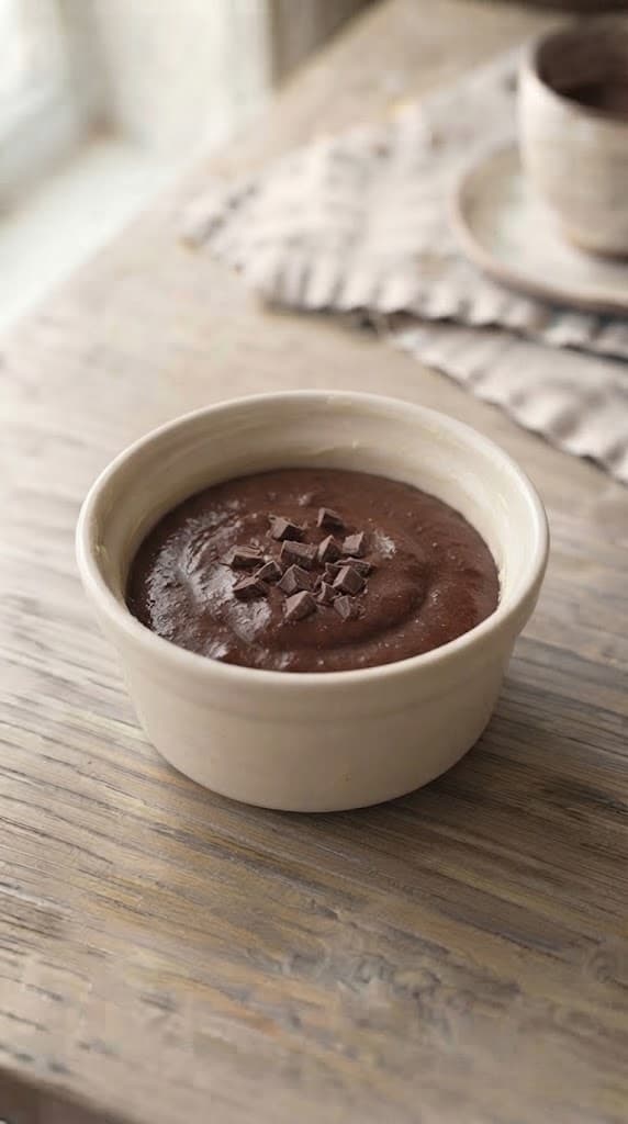 Single-serving chocolate brownie batter smoothed into a small ceramic baking dish with reserved chocolate pieces on top