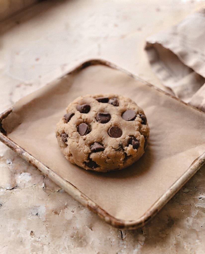 One thick chocolate chip cookie dough round on parchment paper with chocolate on top, ready to bake