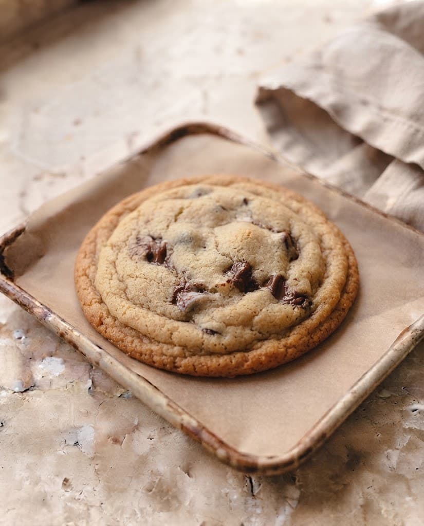 Freshly baked chocolate chip cookie with golden edges and melted chocolate resting after baking