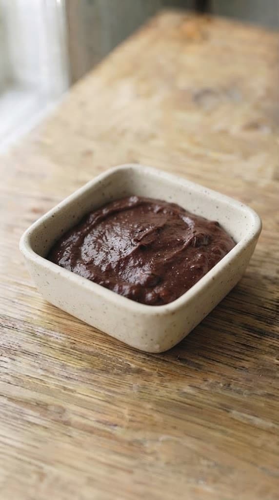 Dark fudgy brownie batter smoothed into a small square ceramic baking dish for one serving