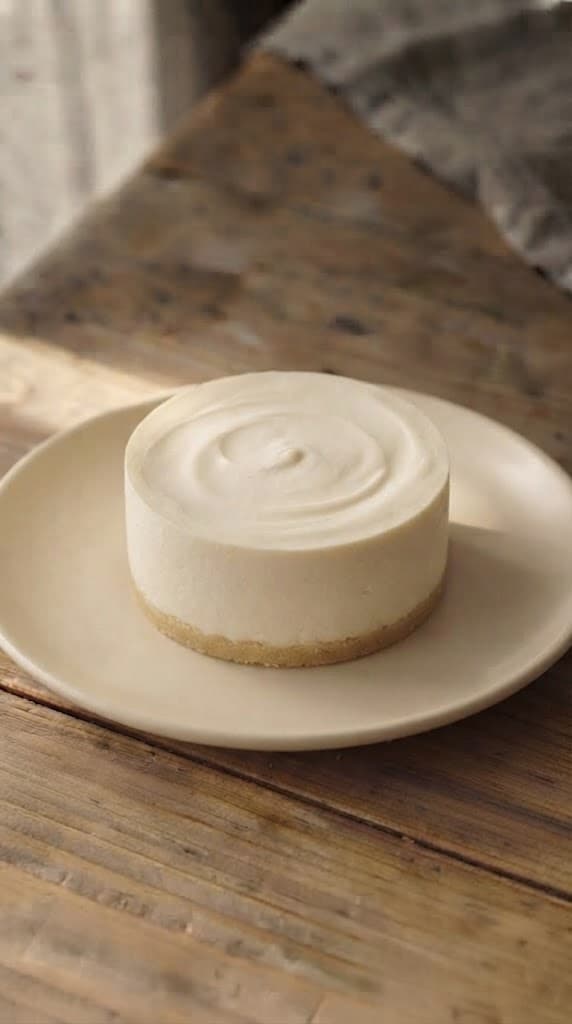 Whole single-serving no-bake cheesecake removed from its mould after chilling with a smooth vanilla filling and thin biscuit crust
