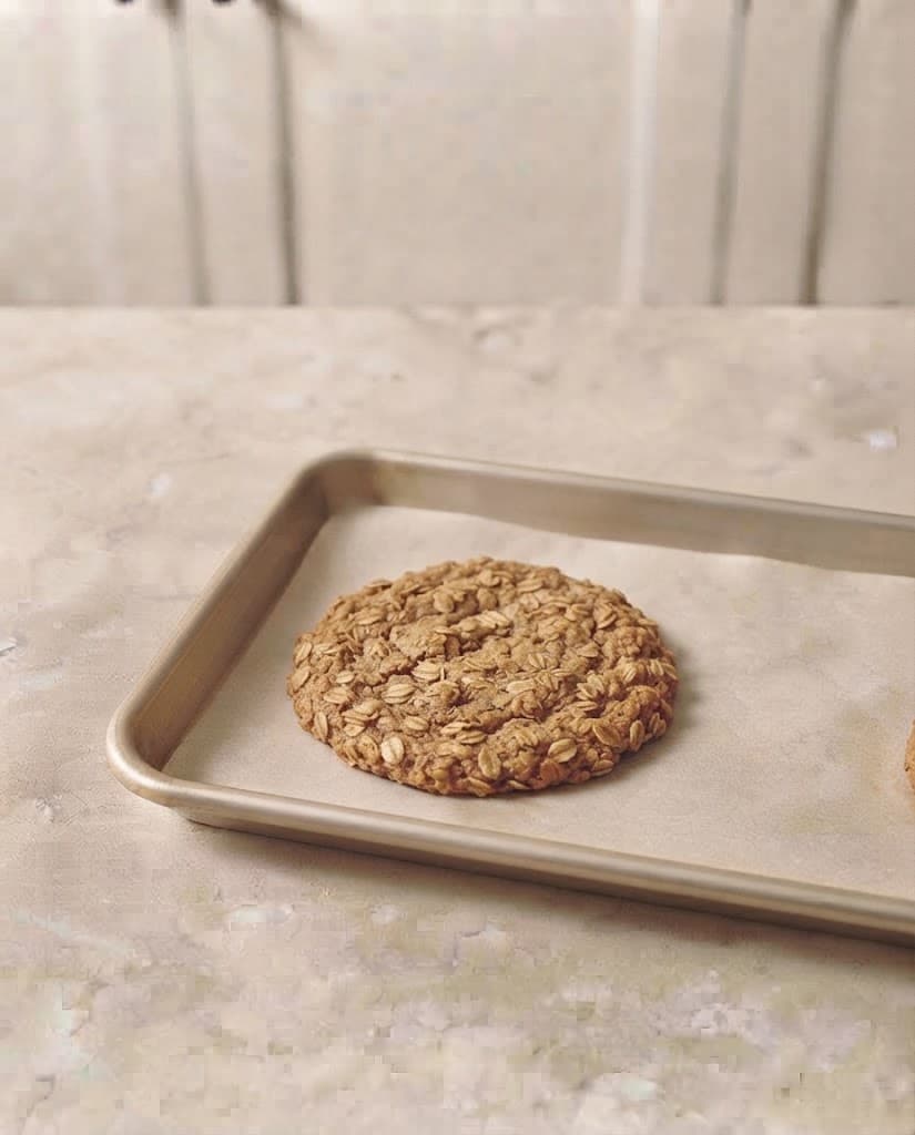 Freshly baked oatmeal cookie with lightly golden edges and visible rolled oats on a parchment-lined baking tray