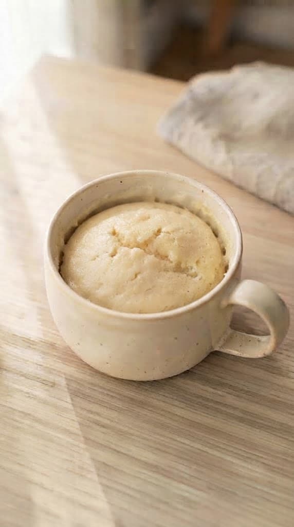 Freshly microwaved vanilla mug cake with a softly risen top and light tender crumb in a cream ceramic mug